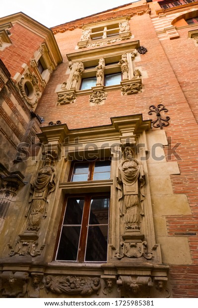 Toulouse, France - Jan. 2020 - Low angle view and\
detail of the richly sculpted brick facade of the luxurious Hôtel\
du Vieux-Raisin, a lordly Renaisance mansion featuring muntin\
windows and statues