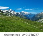 The Tour du Mont Blanc trail, TDMB, leading across lush green mountain meadow with full view of the snow covered Mont Blanc massif in summer in the Chamonix valley in France
