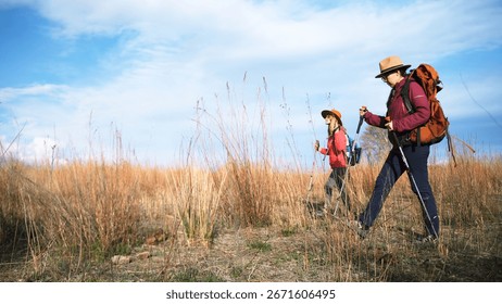 A tour guide and a tour instructor are exploring new routes for commercial hikes. Two women are walking through a field overgrown with tall yellow grass.