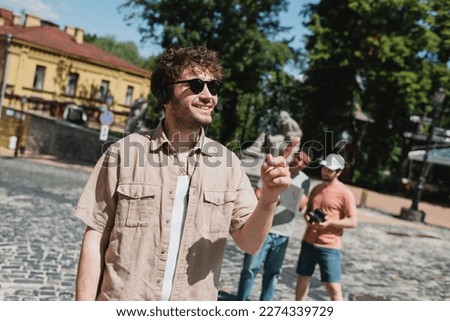 tour guide in sunglasses and headset smiling and pointing with finger near blurred multiethnic tourists on Andrews descent in Kyiv