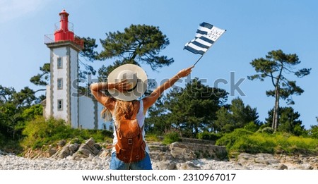 tourism in Brittany- Lighthouse on atlantic coast and woman tourist holding breton flag- Brittany in France (phare de Sainte Marine)