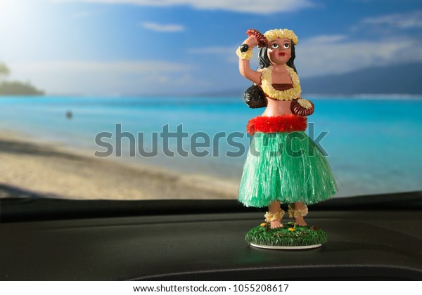 Tourism Concept. Hula dancer doll on\
dashboard car. The car is parking in front of the ocean. The hula\
dance is one of Hawaii\'s oldest\
traditions.