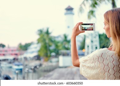 Tourism concept. Young woman  taking photo on smartphone while walking on the seafront. - Powered by Shutterstock