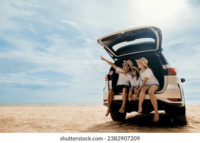 Tourism Day. Dad, mom and daughter enjoying road trip sitting on back car and pointing finger out blue sky, people having fun in summer vacation on beach, Family traveling in holiday at sea beach - Powered by Shutterstock