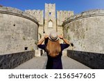 Tourism in Greece. Back view of tourist girl visiting the old Fortifications of Rhodes City, Greece. Unesco world heritage site.