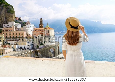 Tourism in Italy. Back view of young woman with straw hat and white dress with Atrani village on the background, Amalfi Coast, Italy.