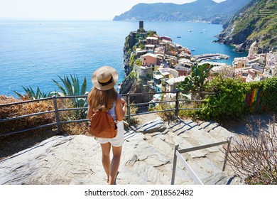 Tourism in Italy. Young female backpacker going downstairs in the Cinque Terre National Park. Beautiful girl walks the Azure Trail and looking at Vernazza town, Italy.