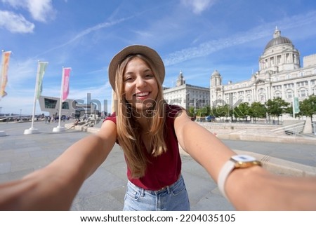 Tourism in Liverpool, UK. Beautiful young woman takes selfie picture in front of Pier Head with 