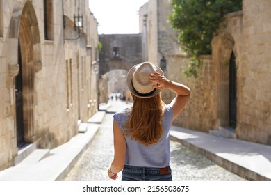 Tourism In Rhodes, Greece. Back View Of Traveler Girl Goes Down The Street Of The Knights Of Rhodes City, Greece. Young Female Traveler Visiting Southern Europe.