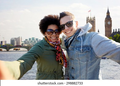 Tourism, Travel, People, Leisure And Technology Concept - Happy Teenage International Couple Taking Selfie Over Houses Of Parliament And Thames River In London Background