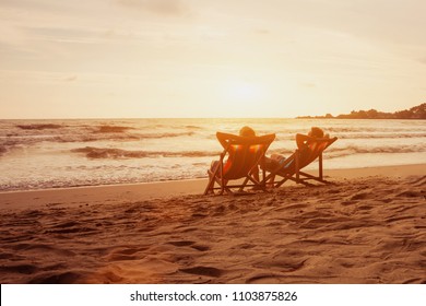 Tourism and travel vacation. Senior happy couple relaxing in luxurious resort sunset beach in deck chairs. Romantic honeymoon holidays. Recreation concept with copyspace.