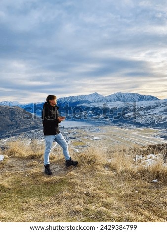 Tourist admires the snowy Remarkables mountain, enjoying the scenic winter view of Queenstown's landscape.