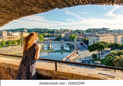 Tourist Admiring View Of Rome From Castel Sant’Angelo, Italy, Europe. Beautiful Panorama Of Roma City, Girl Looks At Rome From Balcony, People Travel In Rome. Sightseeing And Vacation In Italy Theme.