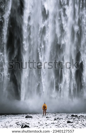 A tourist, adorned in a vibrant yellow raincoat, strolls gracefully from the majestic Skogafoss waterfall in Iceland. The enchanting cascade is located along the Skoga River