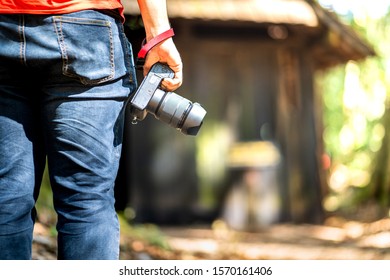 A tourist is adventuring in deep jungle with wooden abandoned house as background. He is holding a camera for taking photo. Urban exploration and outdoor recreation concept. - Powered by Shutterstock