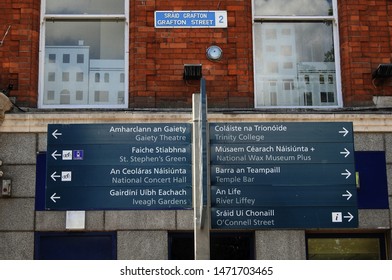 Tourist attractions signpost in English and Irish language, with Grafton Street road sign also in English and Irish language on a wall in the background. 