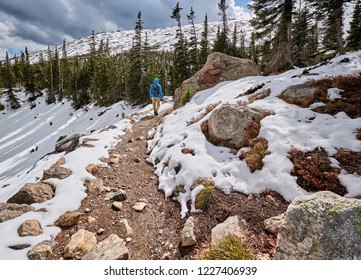 Tourist with backpack hiking on snowy trail in Rocky Mountain National Park, Colorado, USA. 