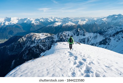 Tourist with a backpack and mountain panorama. Climber in a green jacket climbs a mountain against a blue sky. Hiker with backpack standing on top of a mountain and enjoying view. Adventure concept