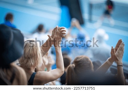 Tourist with backpacks in a crowd watching a sporting event in a stadium. Sports fans cheering and watching tennis at the Australian open in Australia. Hot summer sport fans, wearing summer clothes.