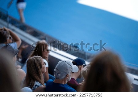 Tourist with backpacks in a crowd watching a sporting event in a stadium. Sports fans cheering and watching tennis at the Australian open in Australia. Hot summer sport fans, wearing summer clothes.