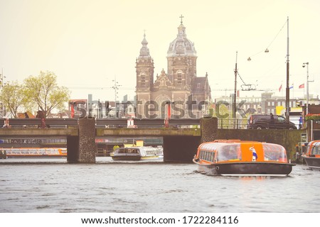 Tourist boat in an Amsterdam canal surrounded with typical Dutch old houses and St. Nicolas Church