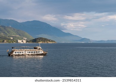 Tourist boats floating on calm Lake Ohrid in North Macedonia. Rolling hills covered in lush green vegetation. Tranquil lakeside scene. Summer travel destination in the Balkans. Boat tour tourism - Powered by Shutterstock