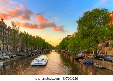 Tourist Canal Tour Boat At Sunset In One Of The Beautiful Canals Of Amsterdam, The Netherlands