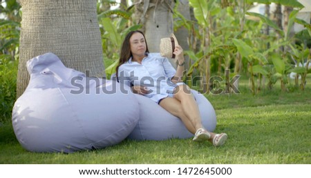 tourist caucasian woman is sitting and relaxing on comfortable pillow chair in tropical garden