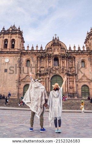 tourist couple celebrating in front of the cathedral in the main square of cuzco wearing sombreros and ruanas