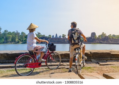 Tourist couple cycling in Angkor temple, Cambodia. Angkor Wat main facade reflected on water pond. Eco friendly tourism traveling.