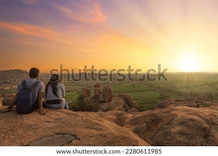 Tourist couple enjoy sunrise from top a hill with scenic landscape view at Hampi Karnataka, India