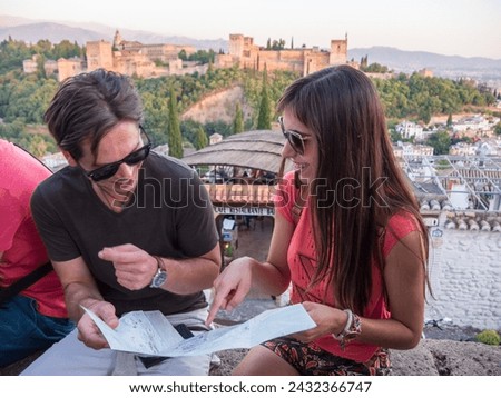 tourist couple man and woman between twenty and thirty years old in front of the alhambra of granada with a map sunglasses and she points