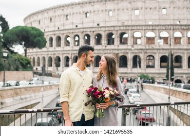 Tourist Couple On Travel Enjoying View On Colosseum In Rome, Italy. Happy Young Romantic Couple Traveling In Europe In Their Honeymoon. Excursion Concept.