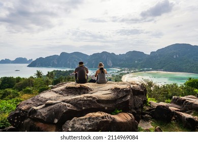 Tourist couple sit on the cliff enjoy amazing view of Phi Phi Don island viewpoint, Krabi, Thailand. Active lifestyle and famous travel destination of Siam.