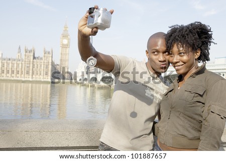 Tourist couple taking a picture of themselves while visiting Big Ben in London city.