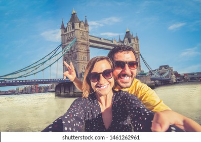Tourist couple travelling in London taking selfie using smart phone with famous Tower Bridge on sunny day seen from Tower of London Area Landmark backgorund having fun summer in England
