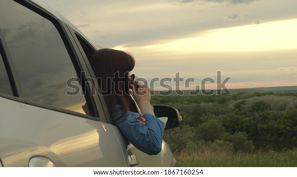 Tourist driver is resting drinking tea from mug in\
sun. Woman traveler holds metal mug with hot coffee in her hands\
and looks at sunset on street next to her car. freedom of travel\
and tourism by car.