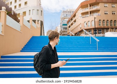 Tourist In Empty City Street. Tourism During Pandemic. Man Walking And Wearing Medical Face Masks Outdoors Next To Blue Steps. Travel Bans Countries Set Limits For Travel Face Masks Mandatory