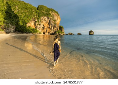 A tourist enjoying the picturesque Phra Nang Cave Beach, Railay in Ao Nang, Krabi, during sunset with stunning limestone cliffs and clear turquoise waters in the background. - Powered by Shutterstock