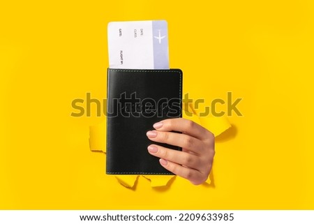 Tourist female hand holding passport with plane ticket isolated through torn yellow background, closeup. Passenger traveling abroad on weekends getaway. Air flight journey concept