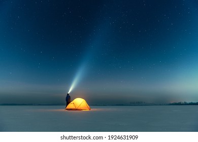 Tourist with flashlight near yellow tent lighted from the inside against the backdrop of incredible starry sky. Amazing night landscape. Tourists camp in snowy field. Travel concept - Powered by Shutterstock