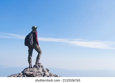 Tourist girl with backpack standing on the stone at the mountain, wear hat and looking panoramic view at Pha Mak Dook Phukradung National park at Thailand.