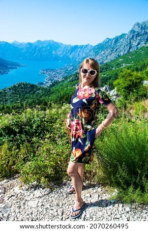 Tourist girl on background on Bay of Kotor (Boka Kotorska), also known as Boka and coastal towns at foot of mountain ranges Pestin Grad. Summer blue landscape. Adriatic Sea. Montenegro.