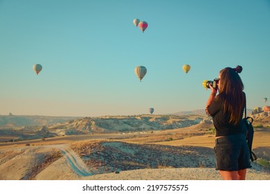 Tourist girl standing and looking to hot air balloons in Cappadocia, Turkey.Happy Travel in Turkey concept. Beautiful brunette Woman  taking photos on a mountain top enjoying wonderful view  - Shutterstock ID 2197575575