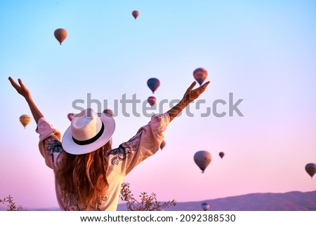 Tourist girl standing and looking to hot air balloons in Cappadocia, Turkey.Happy Travel in Turkey concept.Woman on a mountain top enjoying wonderful view                                