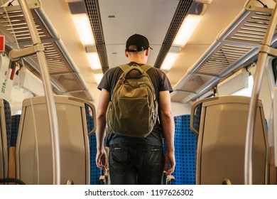 A tourist or a guy with a backpack inside the train is looking for a place to sit down and ride.