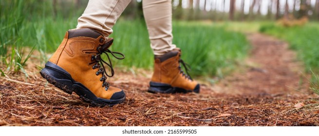 Tourist with hiking boots walking on footpath in forest. Trekking trail in woodland. Waterproof leather ankle boot. Panoramic view