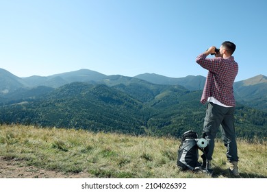 Tourist with hiking equipment looking through binoculars in mountains, back view - Powered by Shutterstock