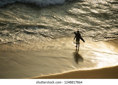 A tourist with his surfboard is on the Varkala beach at sunset ready to enter the sea. India.