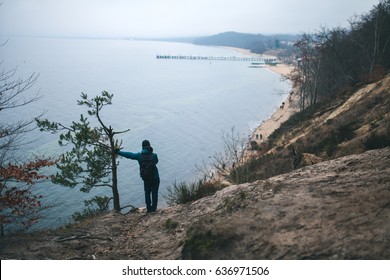 Tourist leaning on the tree at the hill on the Baltic seaside in Winter